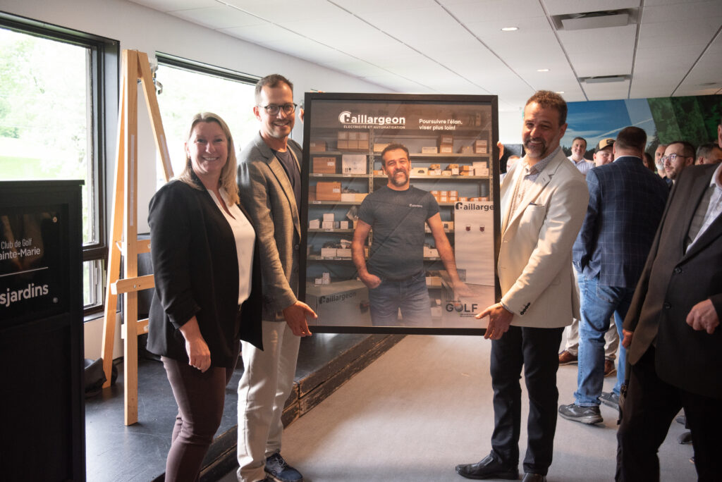 Trois personnes présentent un grand portrait encadré