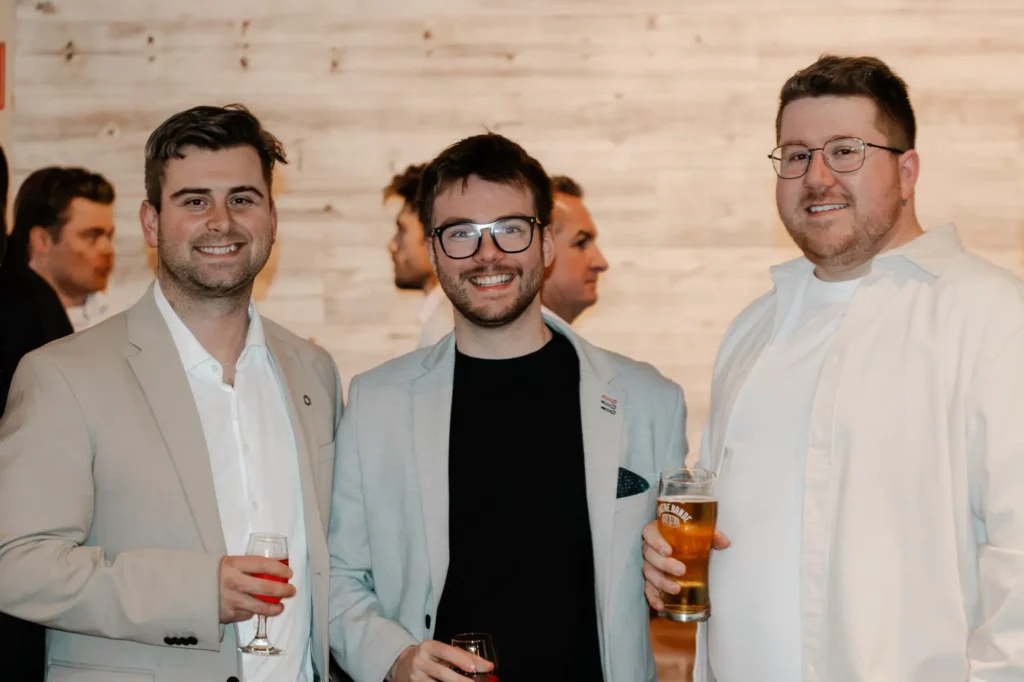 Trois hommes souriants lors d’un événement, verres en main