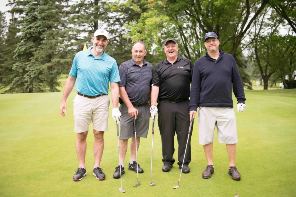 Quatre hommes souriants sur un green de golf