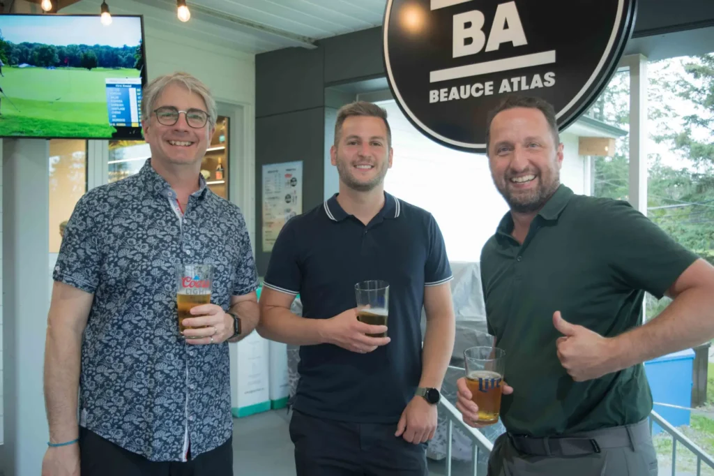 Trois hommes souriants avec bières dans un bar